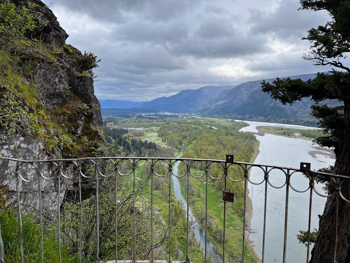 Columbia River wetlands seen past a trail railing and a mossy cliff on Beacon Rock